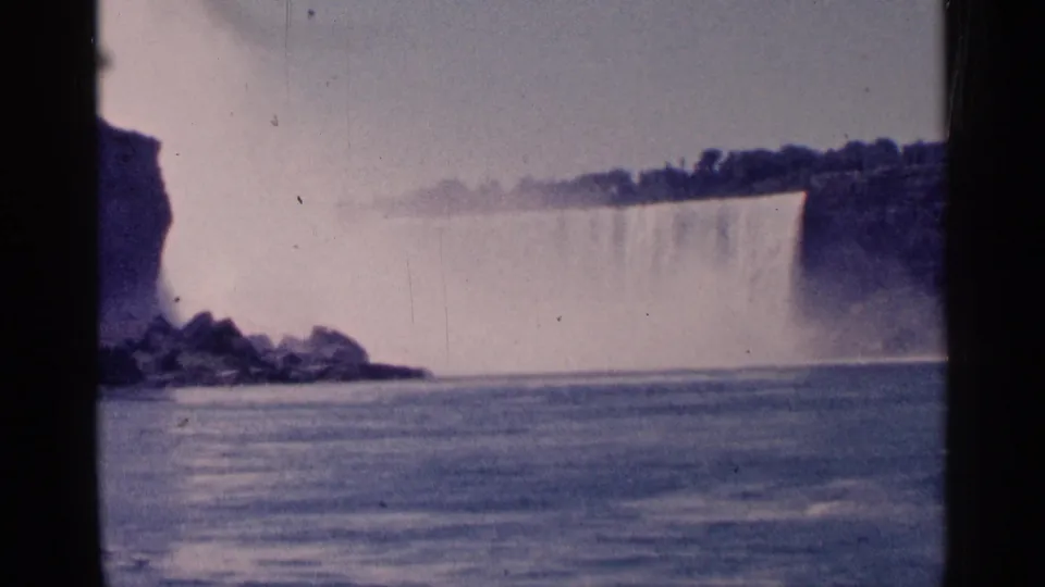 Faded 1964 8mm view of Niagara Falls, with water dropping behind mist and the river filling the foreground.