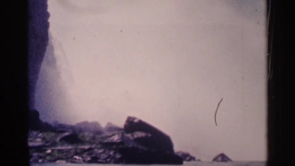 Mist from Niagara Falls rises behind dark rocks, with the cascade partly visible at the left edge in faded 8mm color.