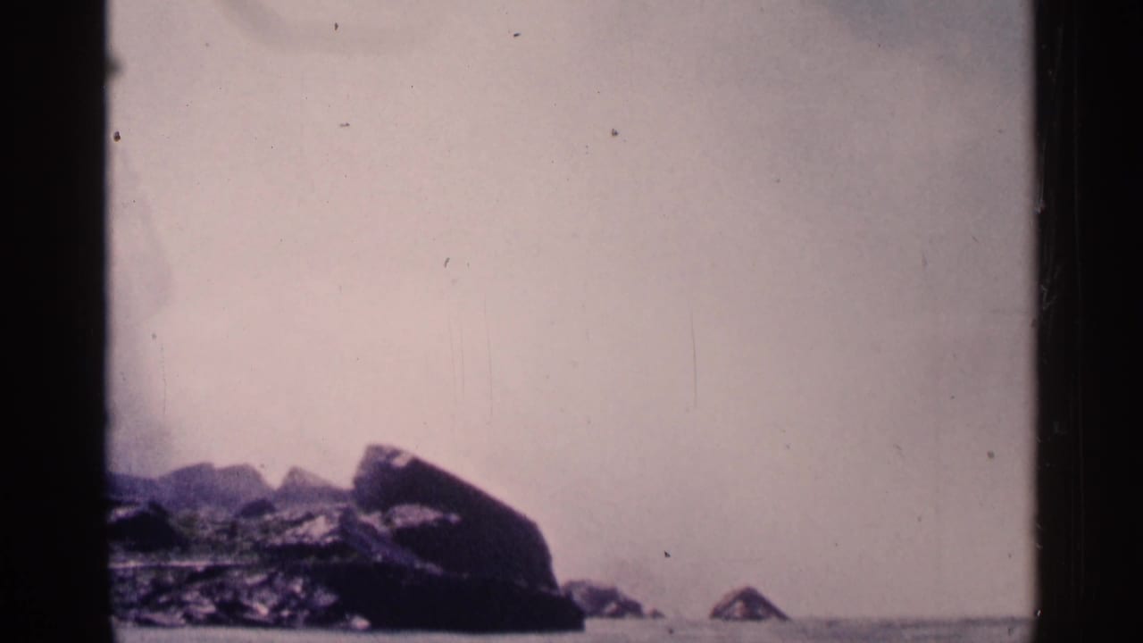 1964 8mm view of Niagara Falls, Canada, with mist over the falls and dark rocky shoreline in the foreground.
