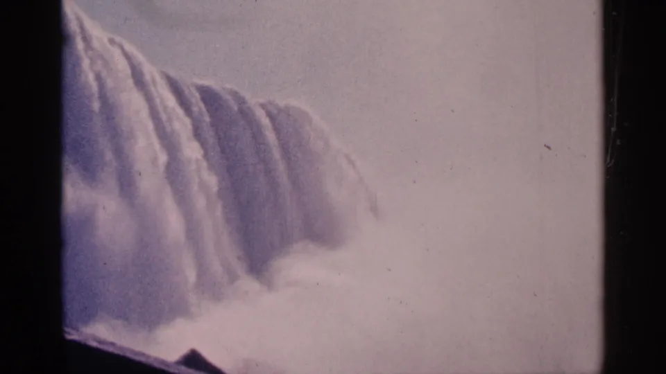 1964 8mm home-movie view of Niagara Falls in Canada, showing a broad cascade and dense mist from a visitor vantage.