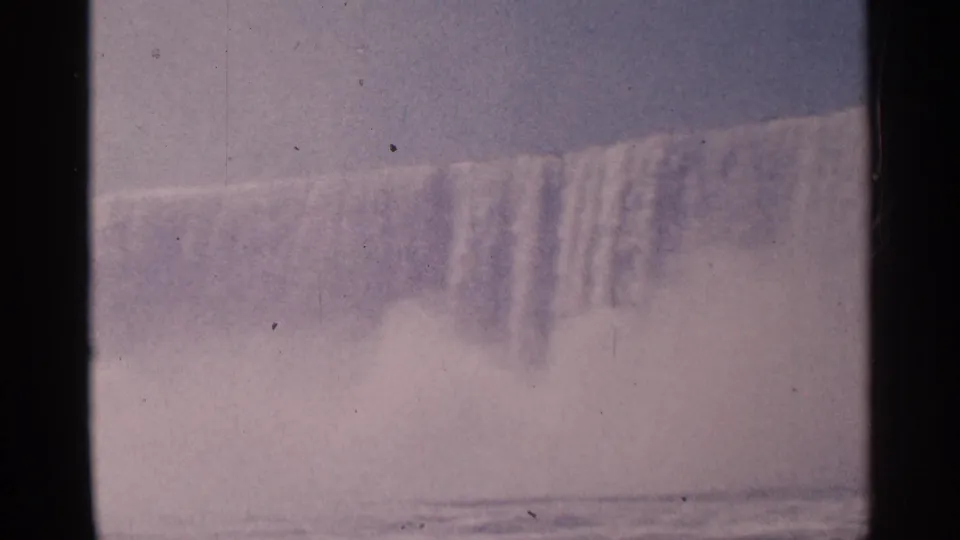 A 1964 8mm view of Niagara Falls shows heavy spray rising in front of the falling water and river surface.
