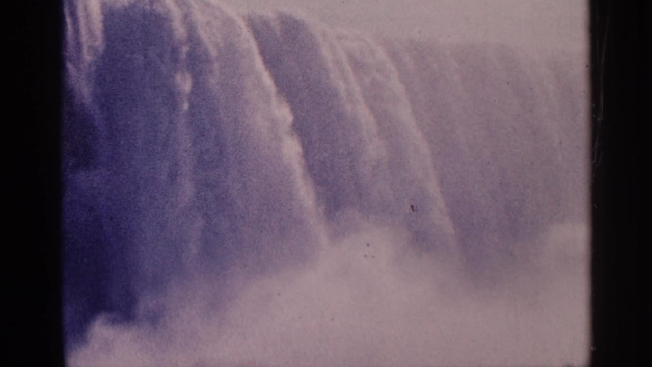 1964 8mm home-movie view of Niagara Falls, Canada, with water dropping through pale mist and faded purple-pink color.