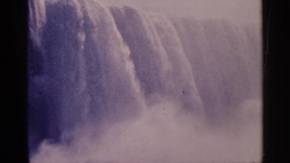 1964 8mm home-movie view of Niagara Falls, Canada, with water dropping through pale mist and faded purple-pink color.