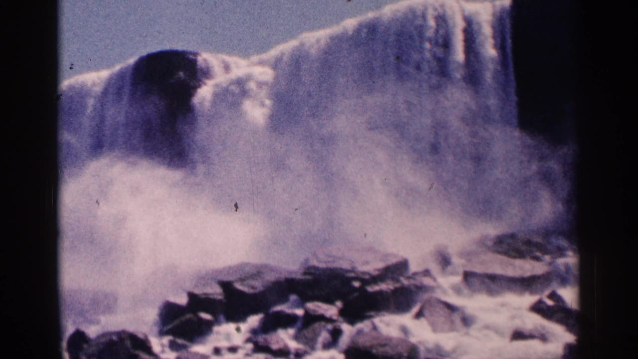 Niagara Falls water drops behind mist with dark rocks at the base.