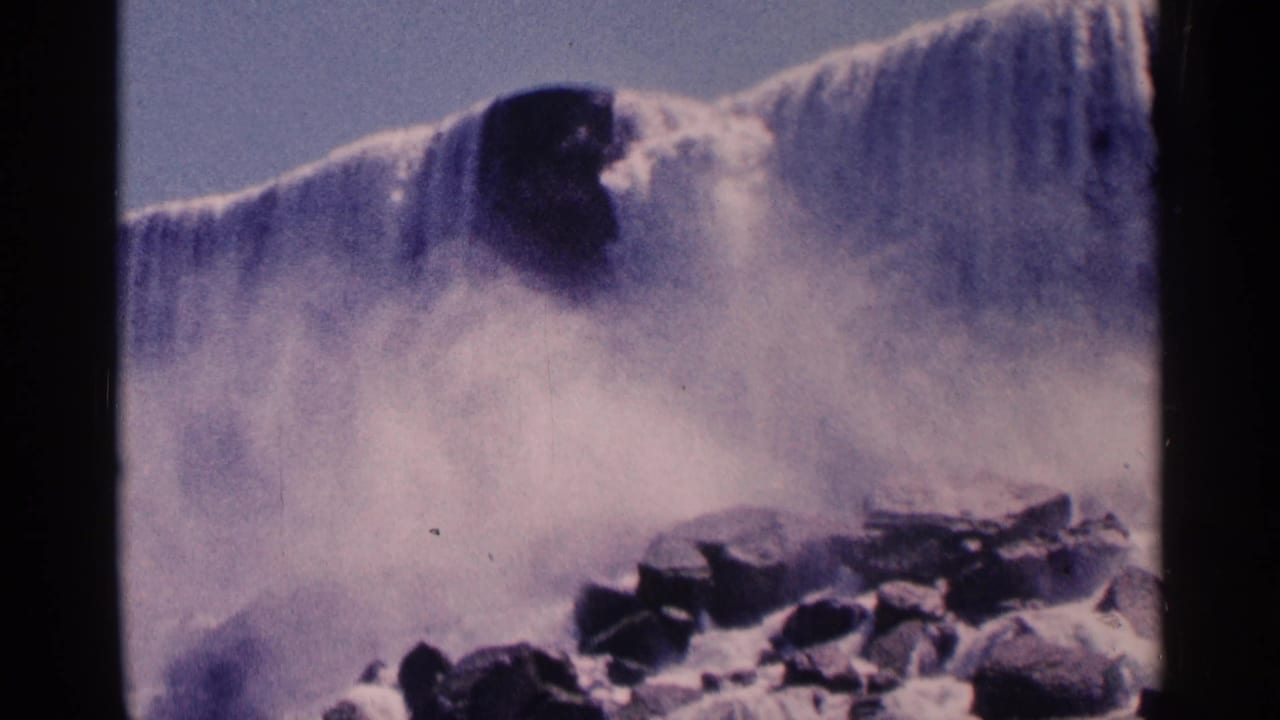 Wide waterfall view with misty spray and rocks below the cascade.