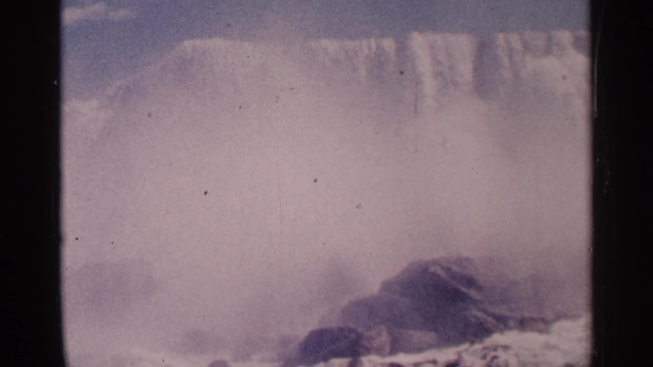 1964 8mm home-movie view of Niagara Falls in Canada, showing pale mist, falling water, rocks, and visible film gate edges.