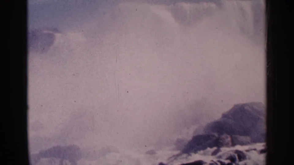 Faded 1964 8mm view of Niagara Falls, with broad mist, turbulent water, dark rocks, and a vertical film-frame divider.
