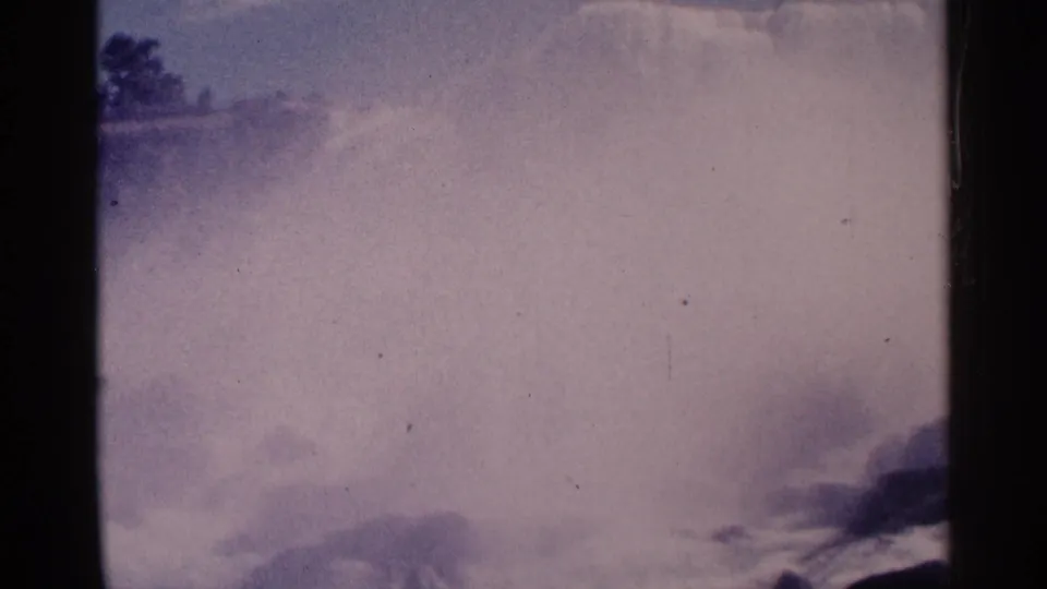 Visitor-shot 8mm footage of Niagara Falls in Canada, showing bright spray, soft water movement, a dark tree edge, and film wear.