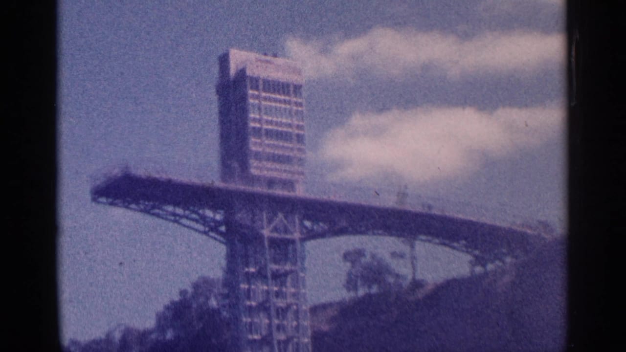 1964 8mm view of a Niagara Falls observation tower with a rectangular upper shaft and broad deck under clouds.