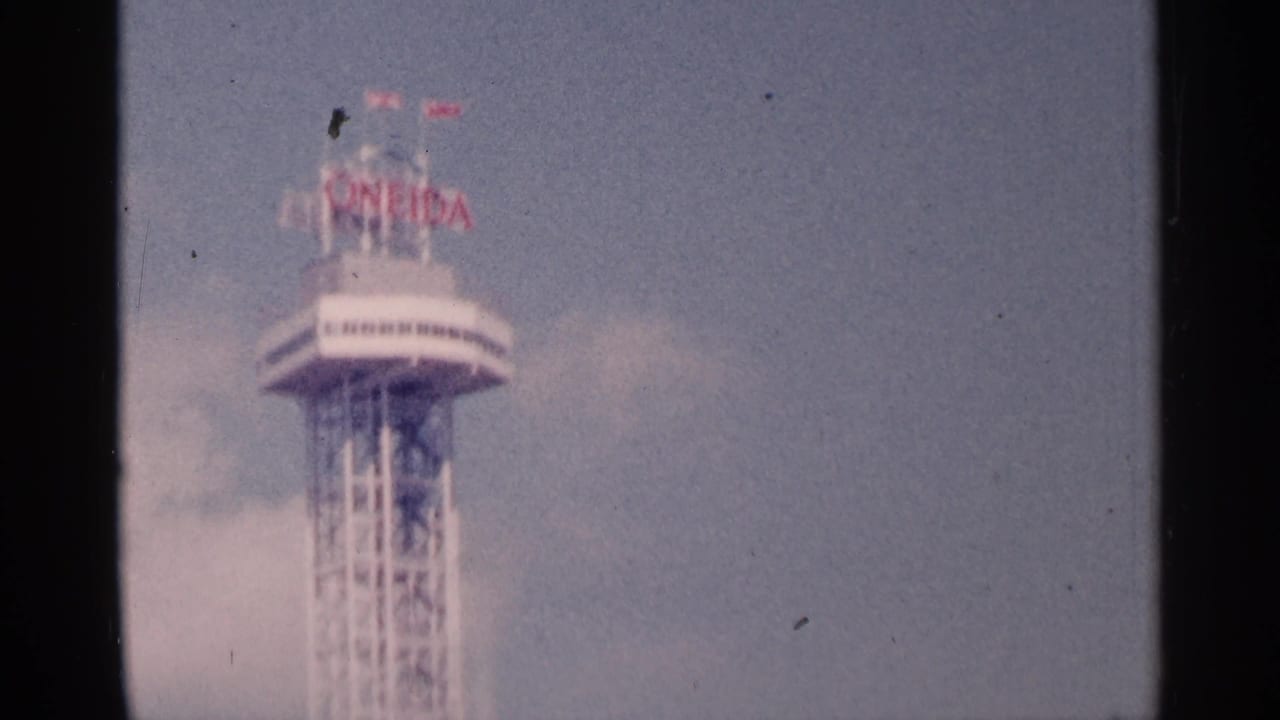 Tall skeletal tower with circular top and red signage against a pale sky.
