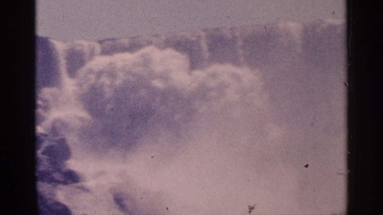 1964 8mm home-movie frame showing a close view of Niagara Falls cascade, mist, and aged purple-pink film color.