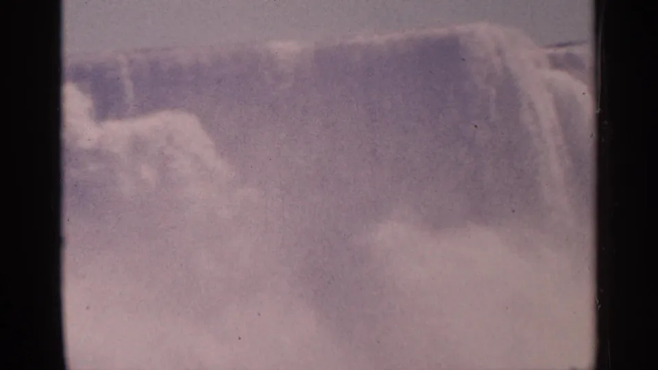 Close 1964 Niagara Falls view with water dropping over the brink, dense spray, dark frame edge, and aged 8mm color cast.