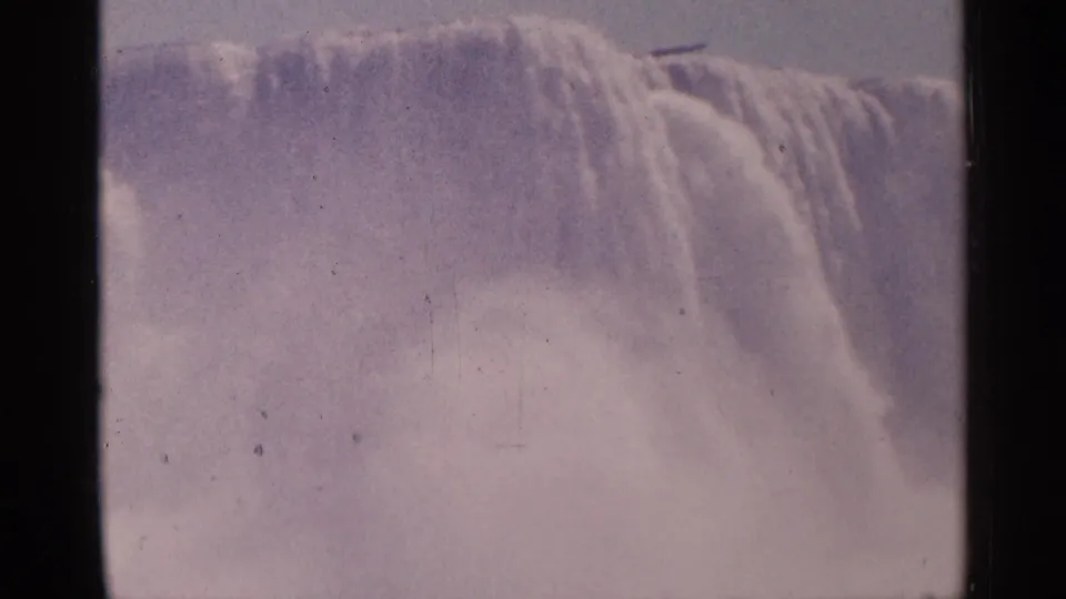 1964 home-movie frame of Niagara Falls water sheeting downward, with mist filling the lower frame and visible 8mm grain.