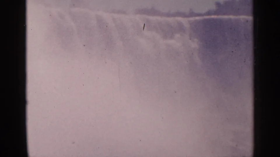 A soft, grainy 8mm frame of Niagara Falls, Canada, with pale water, drifting mist and visible film wear.