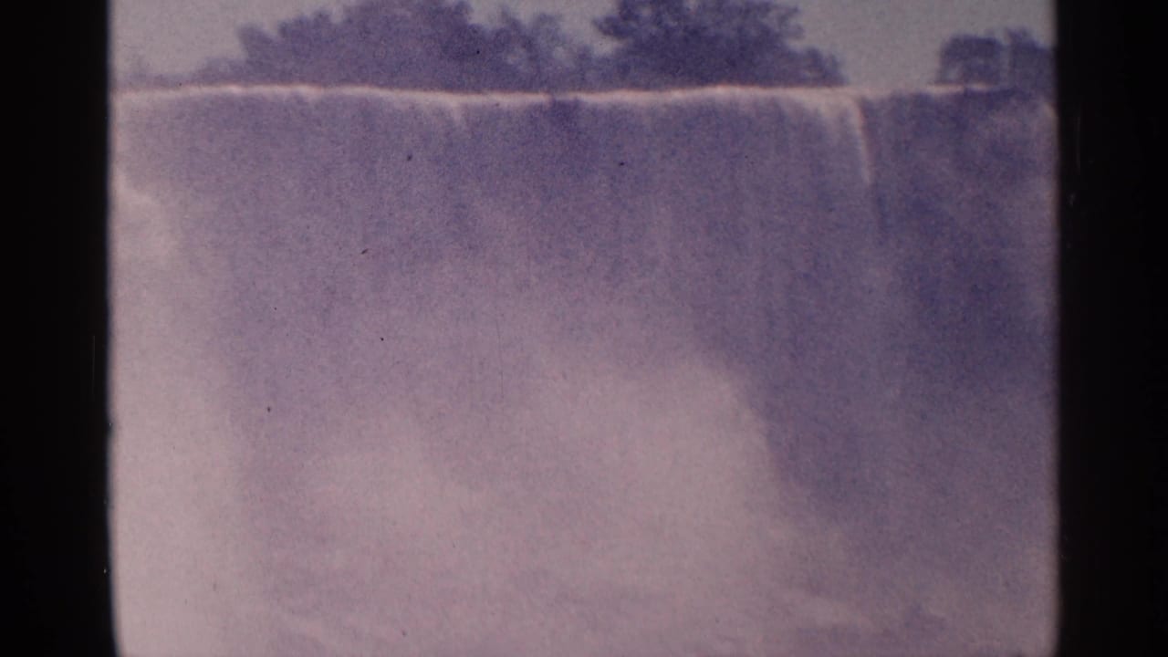 Wide hazy view of a large waterfall with mist and dark tree line above.