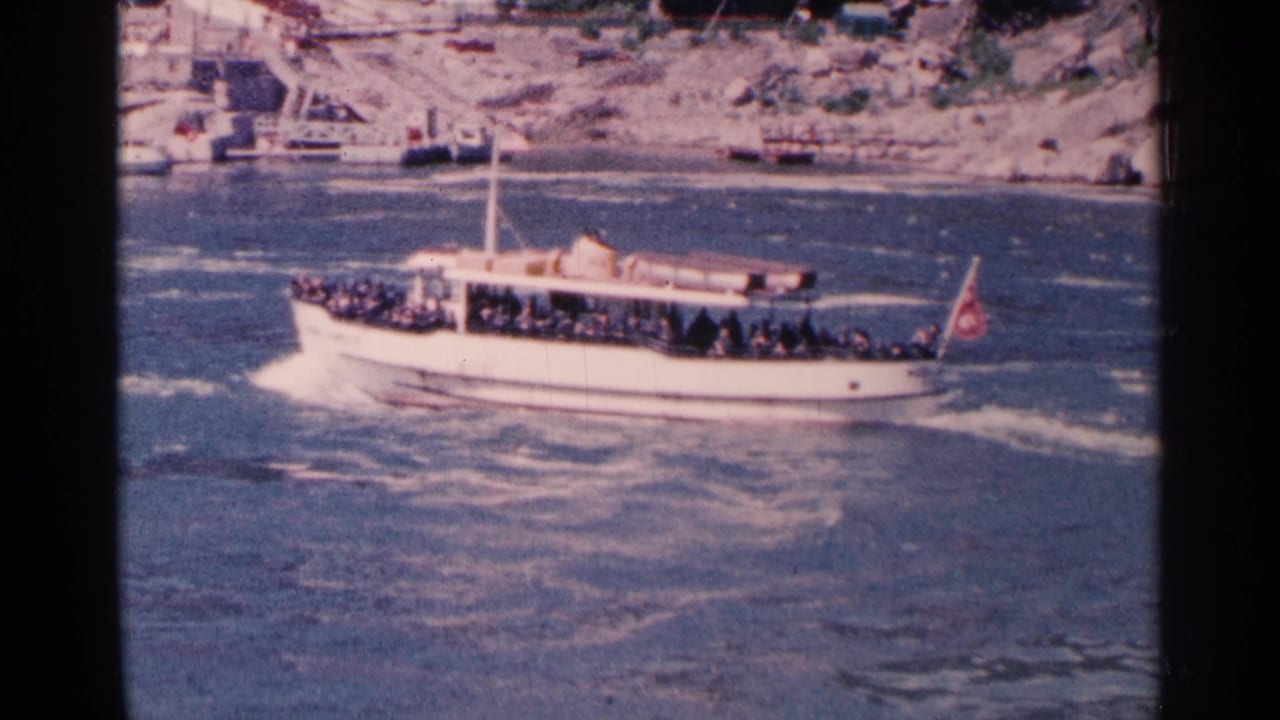 White sightseeing boat with passengers cuts across blue-green river water.