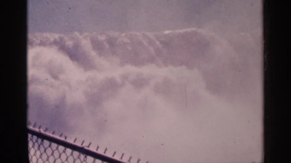 1964 Niagara Falls, Canada frame showing the falls through thick mist from behind a chain-link viewing fence.