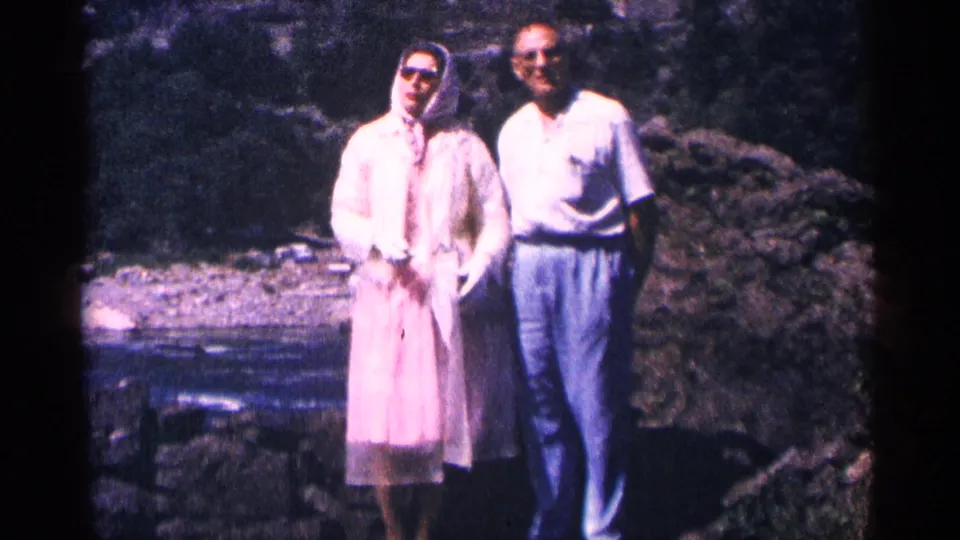 The couple remains near Niagara Falls in a soft 8mm frame, the woman in pink rainwear and the man standing close beside her.