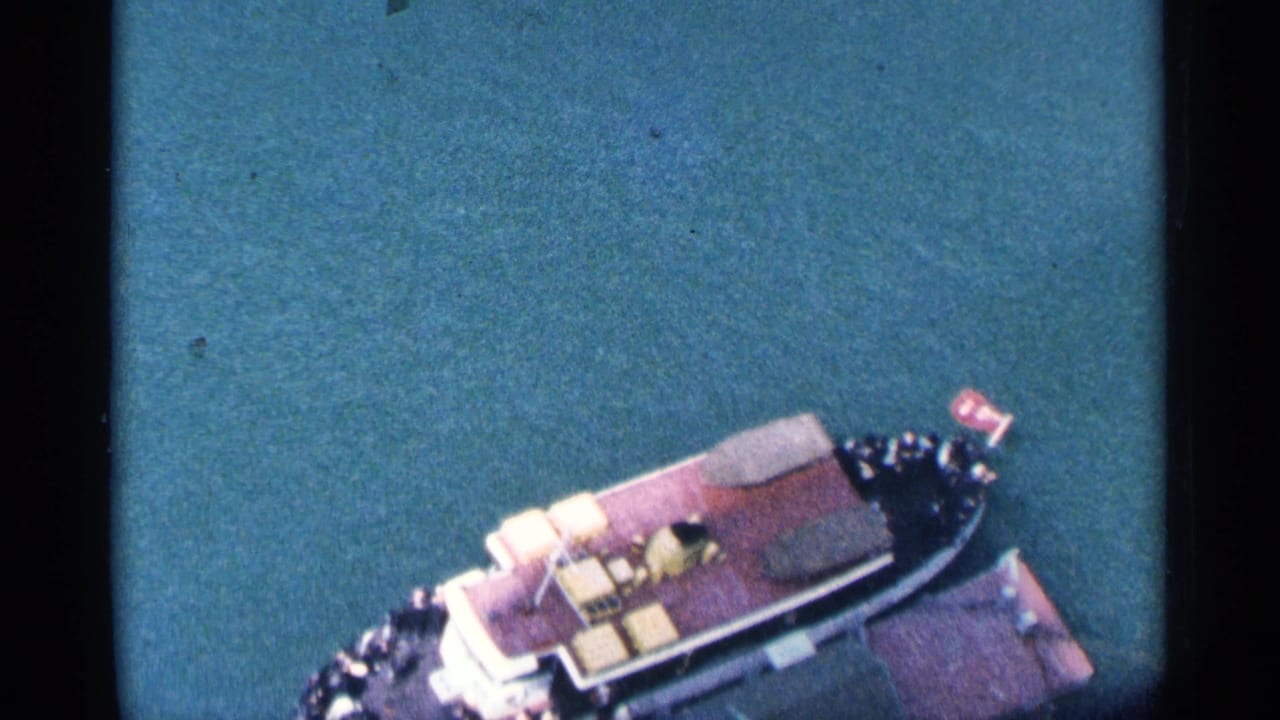 Small passenger boat seen from above on blue-green water.