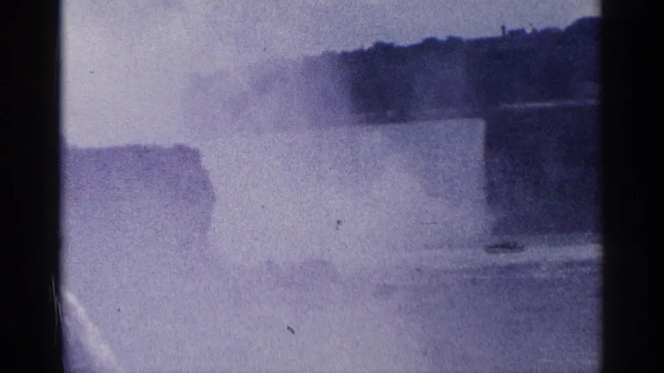 1964 Niagara Falls home-movie frame showing mist over water near the falls, with dark shoreline forms in the background.