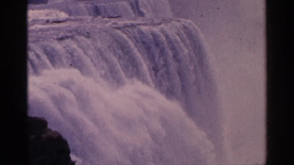 1964 8mm view of Niagara Falls water plunging downward, tinted purple with visible grain and frame edge shadow.