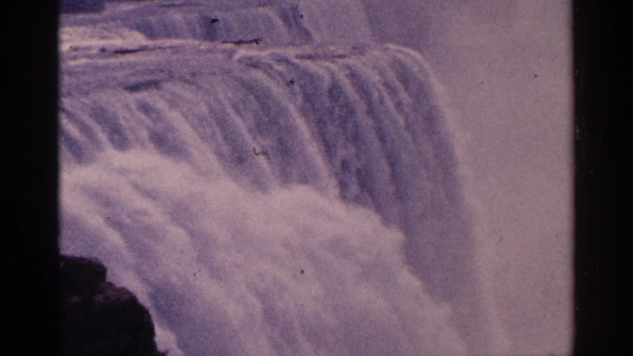 Purple-tinted 8mm frame showing Niagara Falls water dropping in a broad curtain with mist and light scratches.