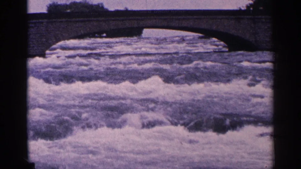 Vintage 8mm frame of turbulent water beneath a bridge at Niagara Falls, Canada, with purple cast and soft archival texture.