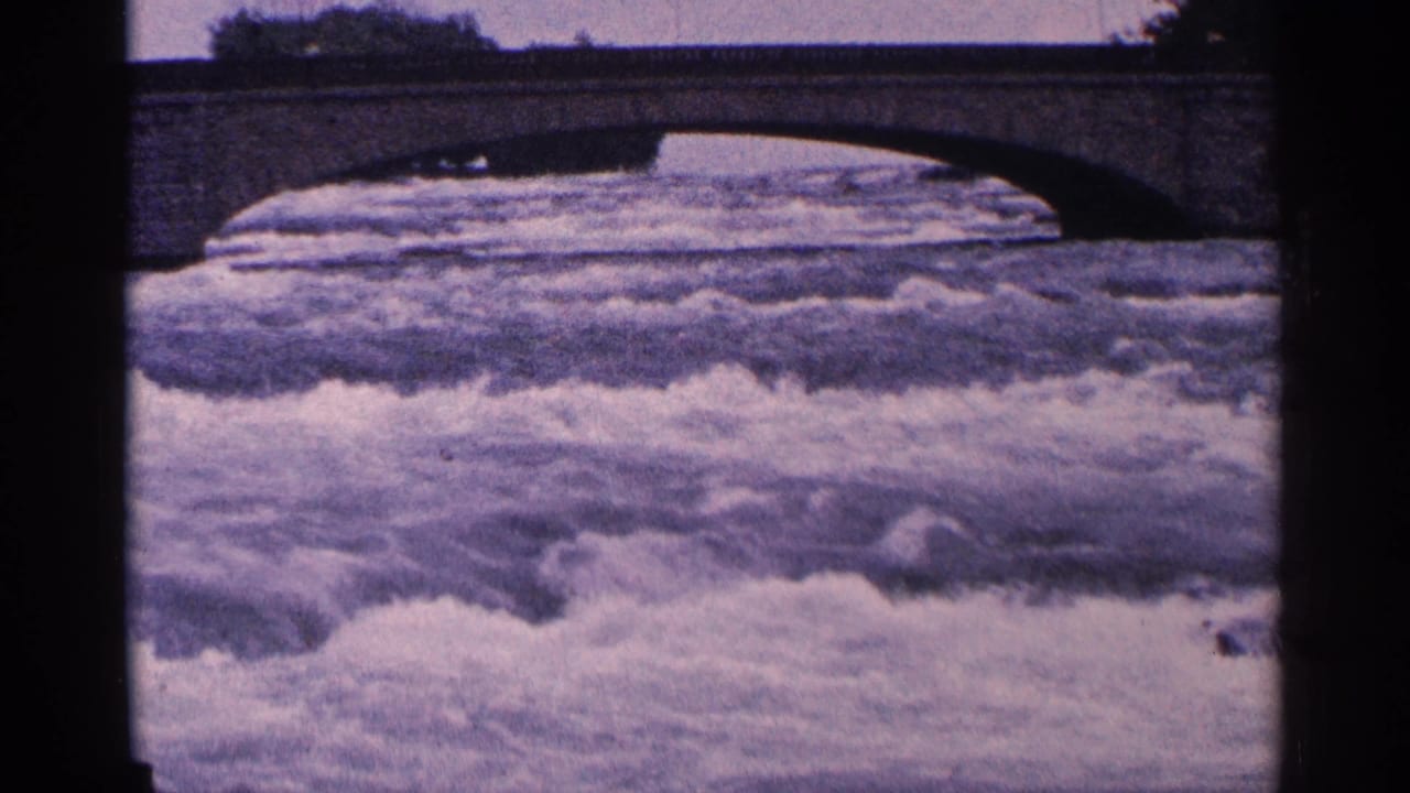 White rapids rushing beneath a stone arch bridge with dark 8mm film borders.