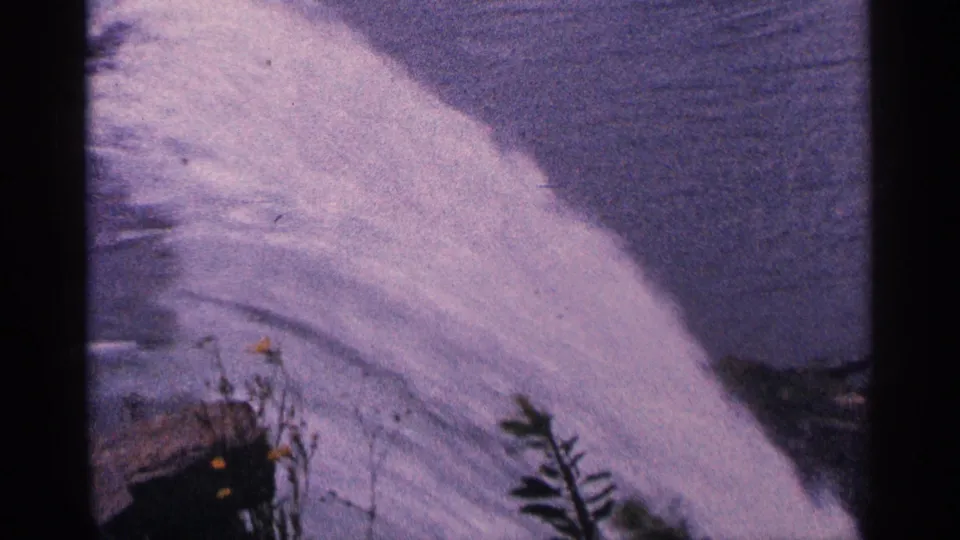 Aged 8mm footage of Niagara Falls in 1964 shows white water spilling past rocks and sparse vegetation.