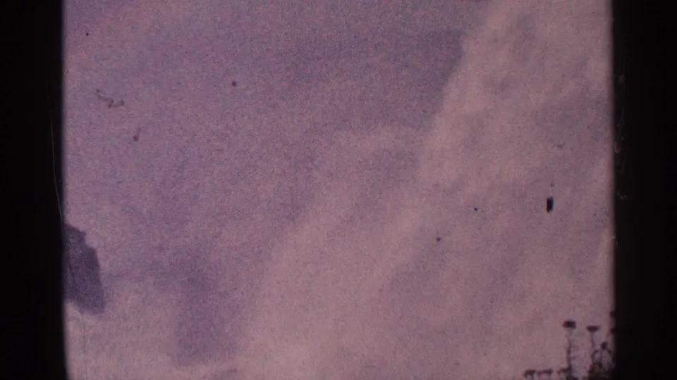Soft, faded 8mm frame of Niagara Falls mist and sky, with small shoreline structures or figures barely visible at the edge.