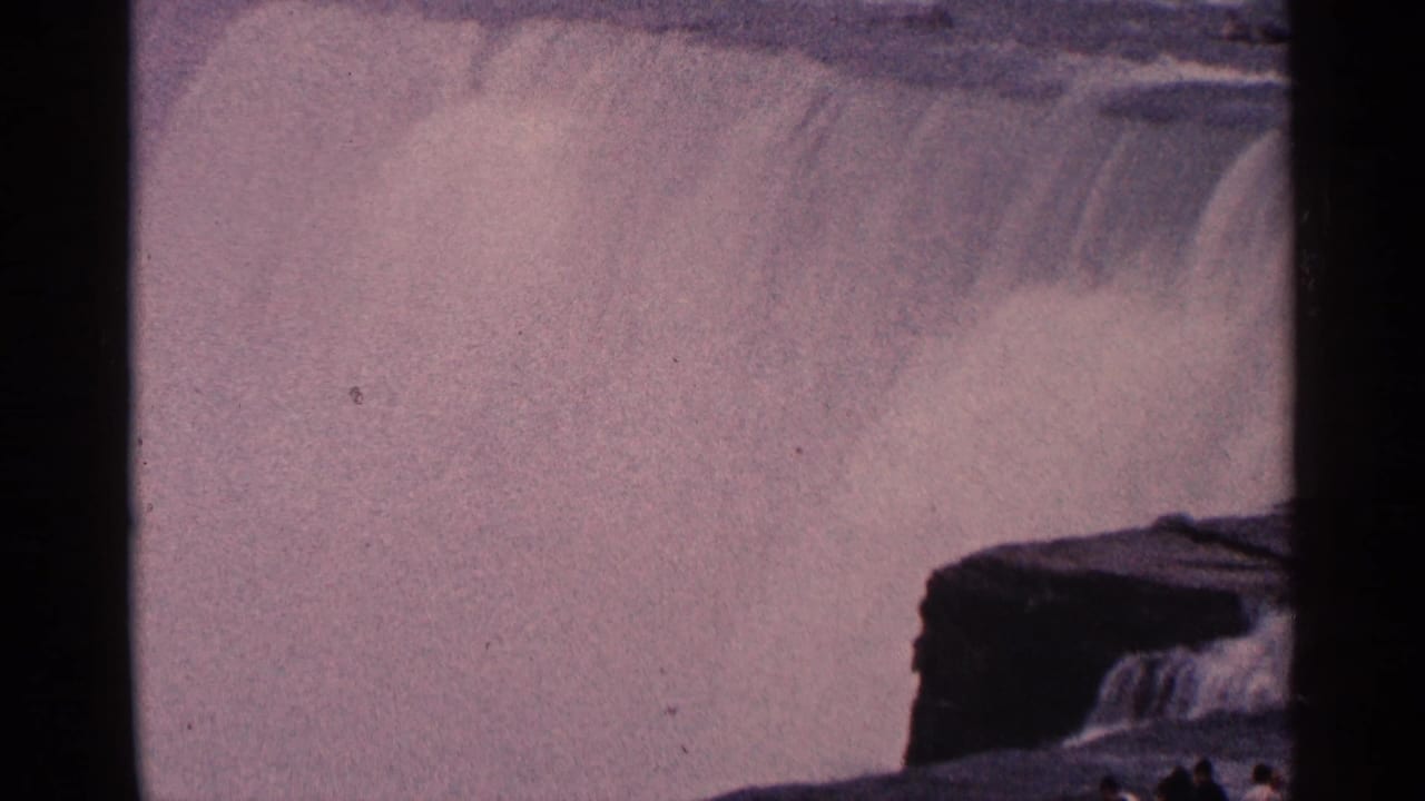 1964 8mm home-movie frame of Niagara Falls, Canada, showing water dropping over a dark ledge into dense spray.