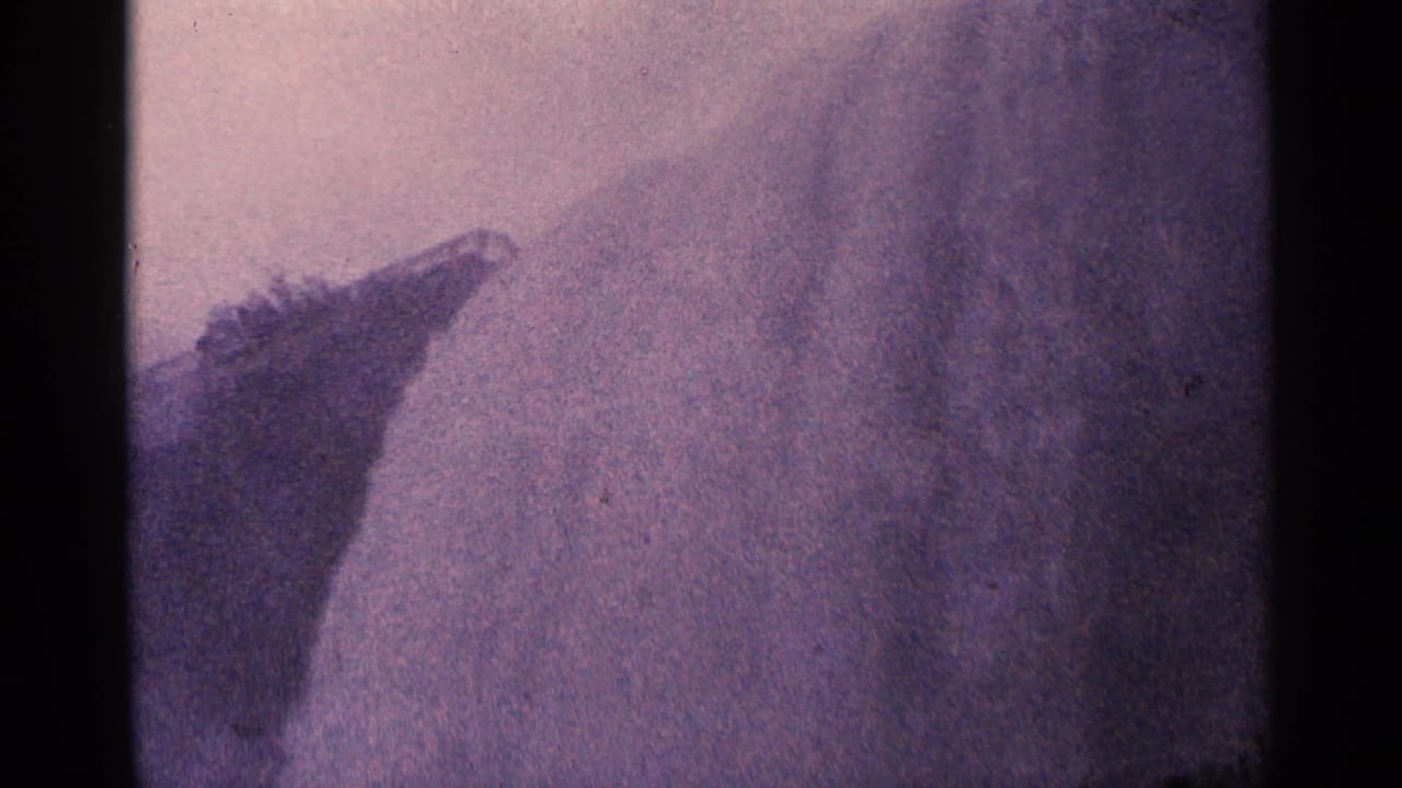 A large wall of mist and falling water fills the frame beside a dark rocky edge.
