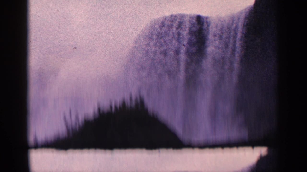 1964 Niagara Falls home-movie frame with the waterfall partly obscured by a dark shoreline or treetop silhouette in the foreground.