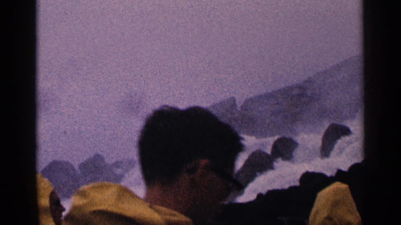 1964 Niagara Falls home-movie frame showing mist, dark rocks, rushing water, and visitors close to the shoreline.