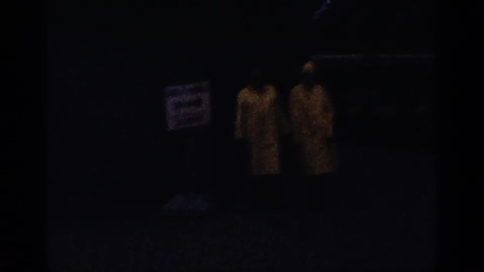 Dark 1964 Niagara Falls frame with two adults in yellow raincoats walking near a posted sign and wet path.
