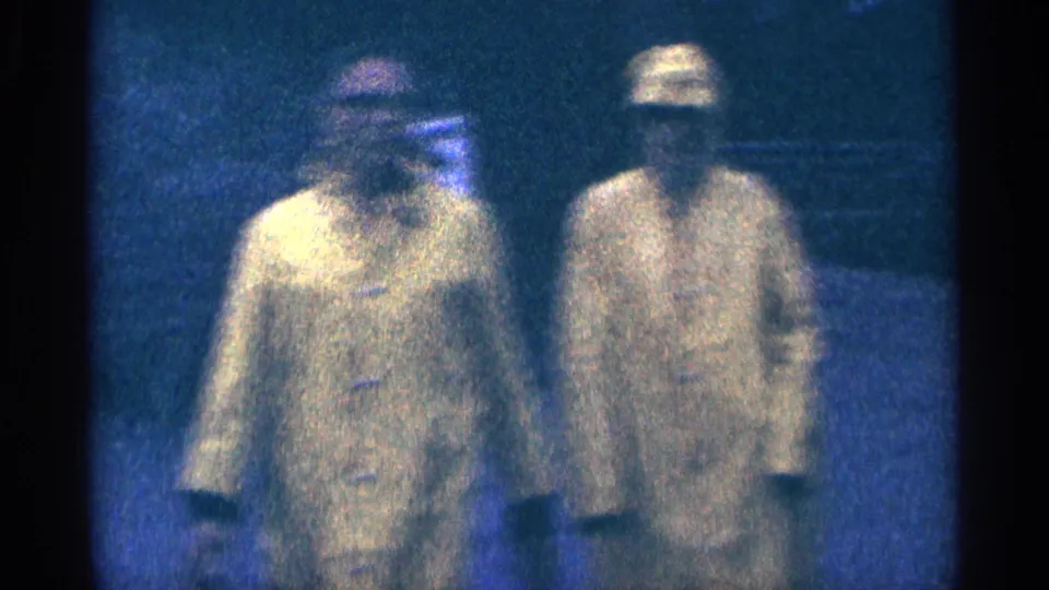 Close low-light view of two adults in yellow raincoats walking toward the camera in 1964 Niagara Falls home-movie footage.