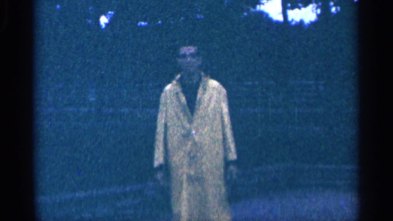 Man in a yellow raincoat standing on a park path.