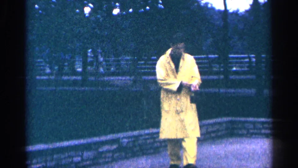 A man in a yellow raincoat walks along a paved park path beside a low stone wall in the Niagara Falls travel footage.