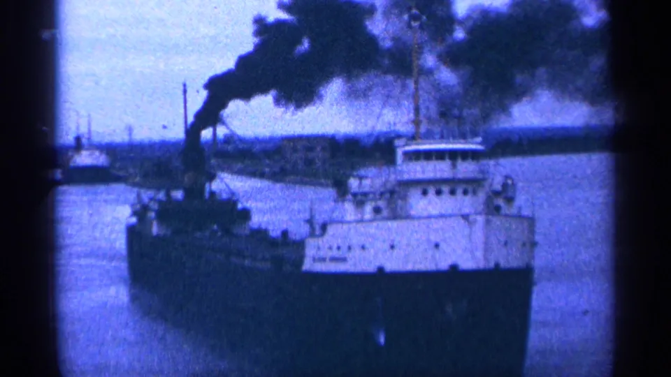 A large freighter sits or moves on the water as thick black smoke rises from the stack in the 1964 travel reel.