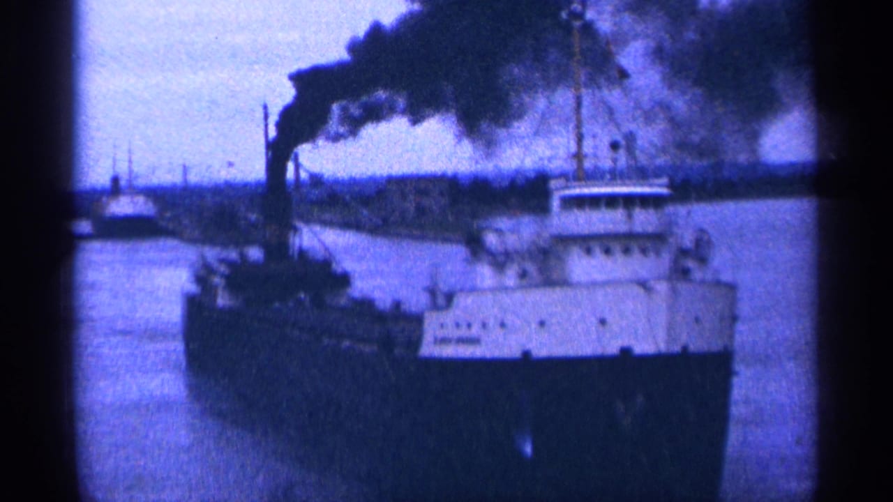Large ship on a waterway with dark smoke rising from its smokestack.