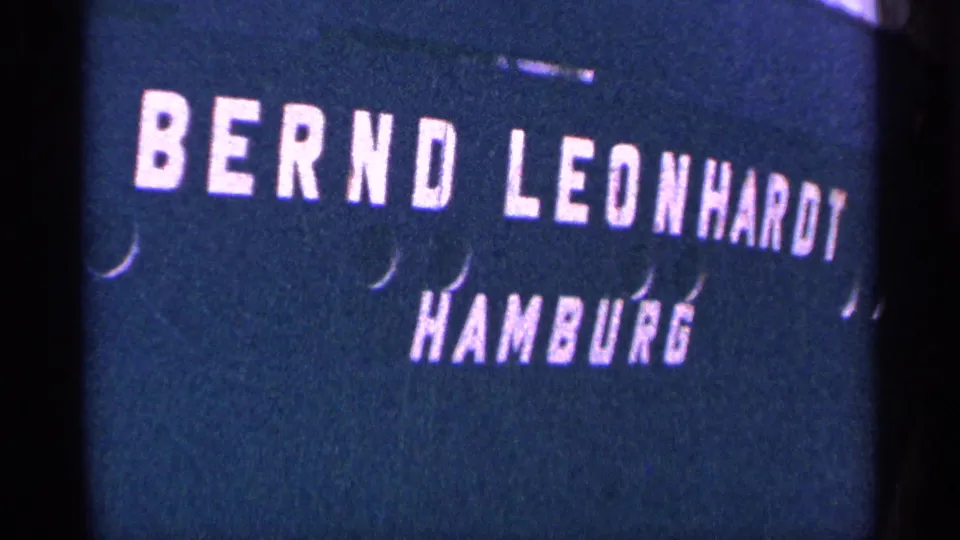 Close 8mm frame of a dark title card bearing the white block text Bernd Leonhardt and Hamburg, with visible grain and edge shadowing.