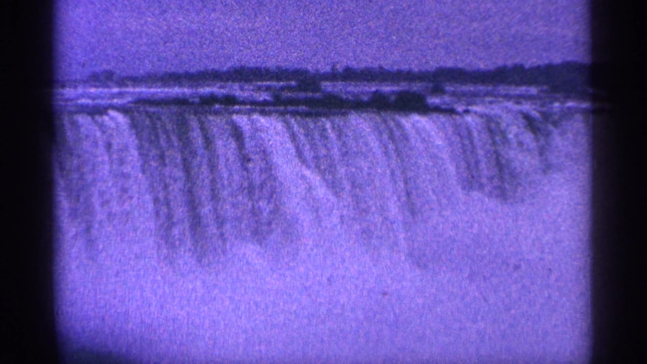 Wide purple-tinted view of water dropping over Niagara Falls.