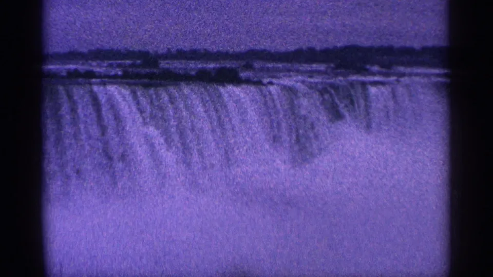 Wide 1964 8mm shot of Niagara Falls, with the falls' edge, falling water, mist, and distant shoreline visible.