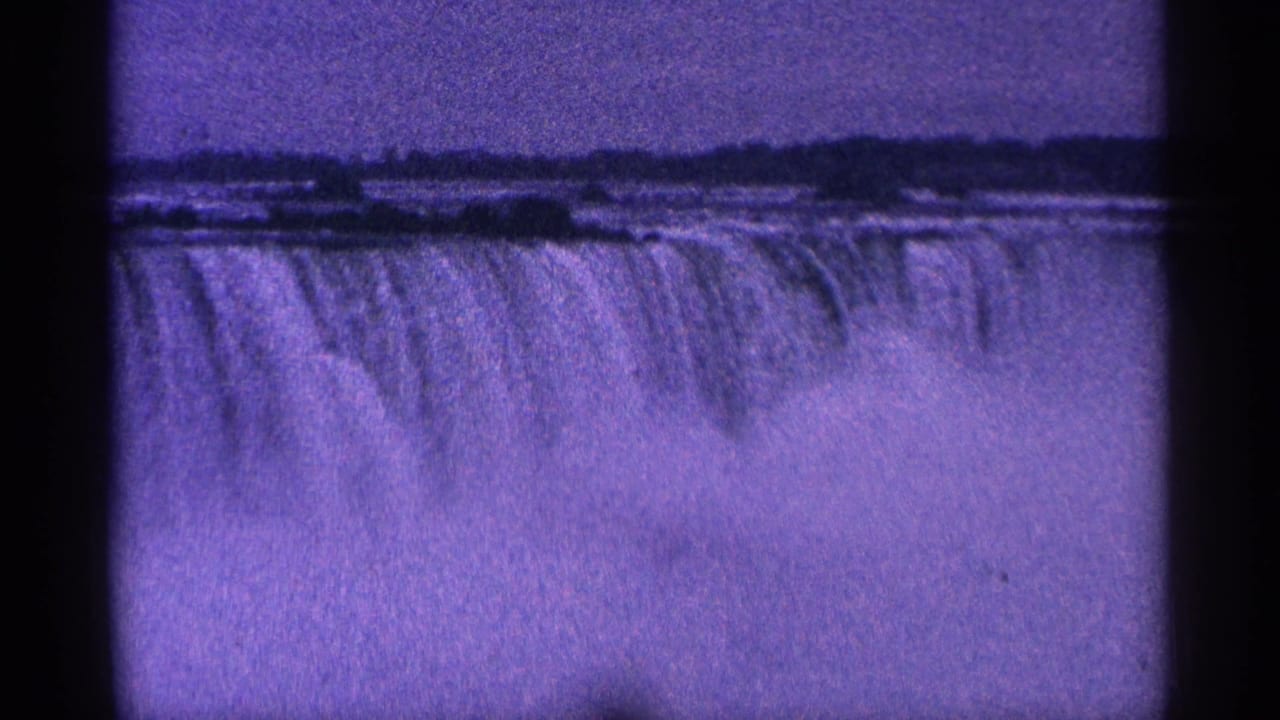 Wide purple-tinted view of Niagara Falls with mist, treeline, and black film borders.
