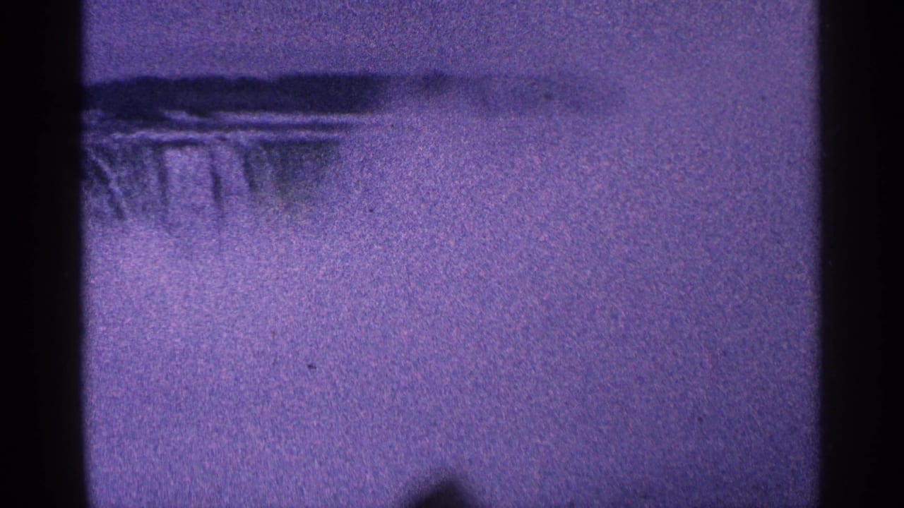 Purple-tinted mist and falling water framed by dark film edges.