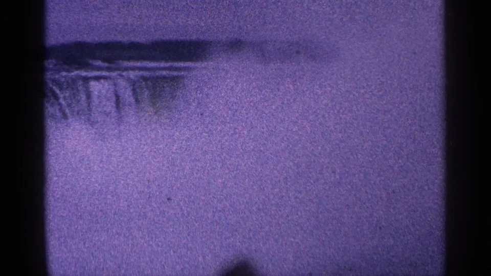 1964 8mm home-movie frame of Niagara Falls, Canada, with misty falling water, purple tint, grain, and dark gate edges.