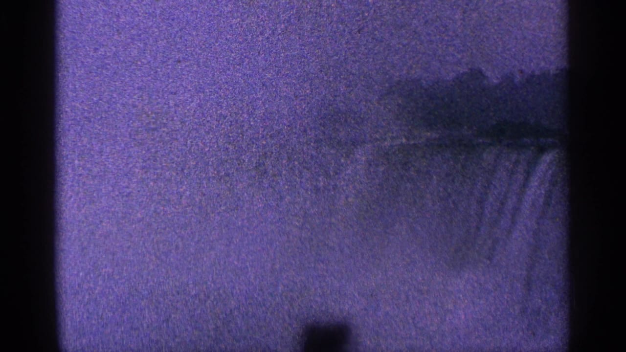 1964 8mm frame of Niagara Falls, Canada, seen through soft focus, heavy grain, and dark vertical film-edge obstruction.