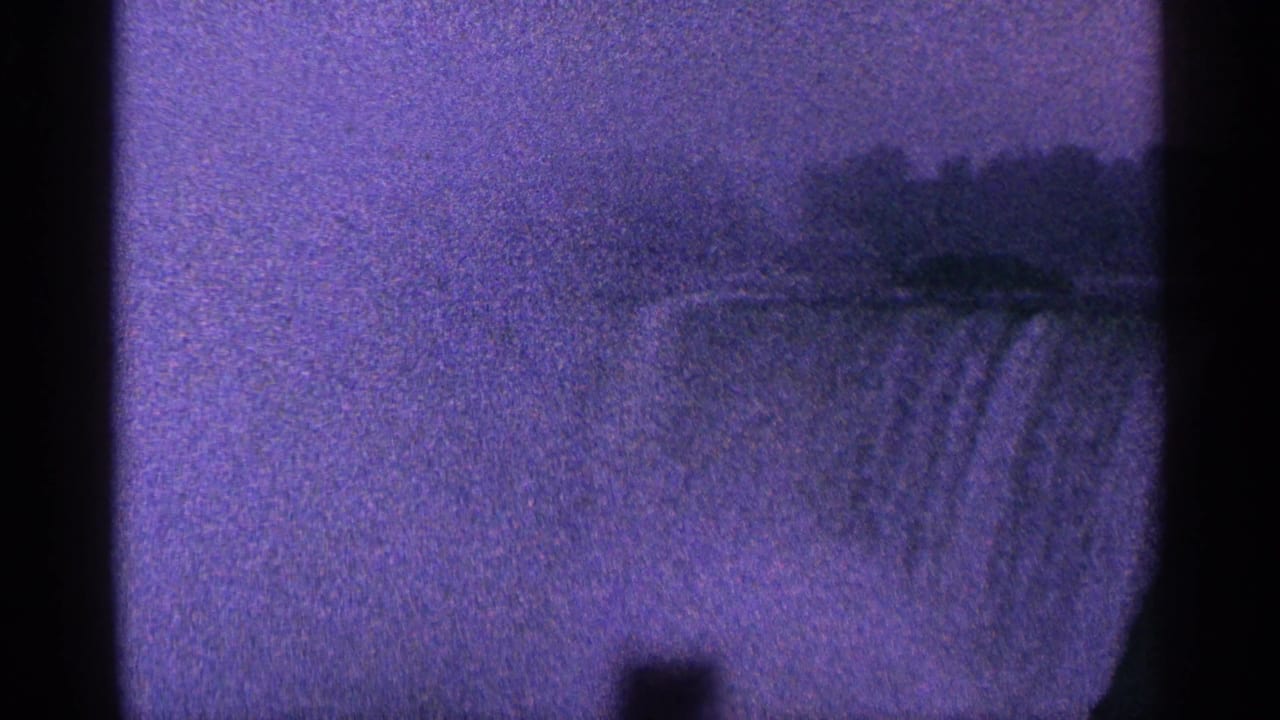 Grainy waterfall view with a dark vertical strip and hazy treeline above the falls.