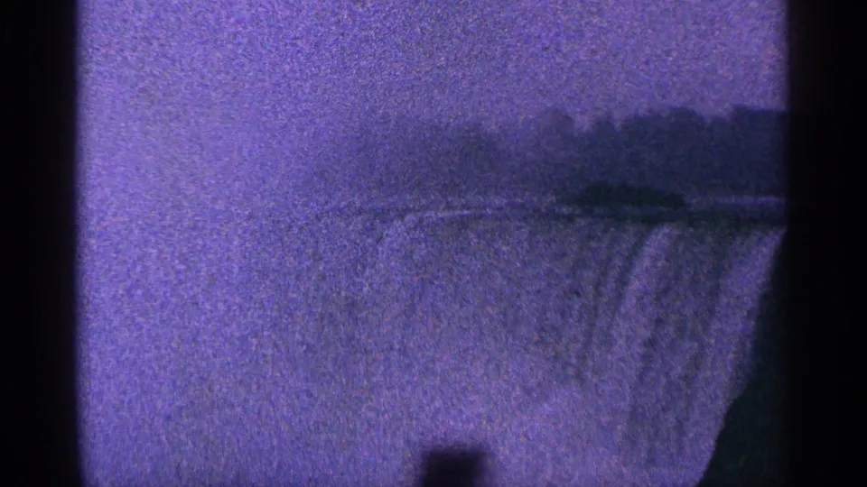 1964 home-movie frame of Niagara Falls, Canada, with the cascade partly visible below a dark, hazy landscape line.