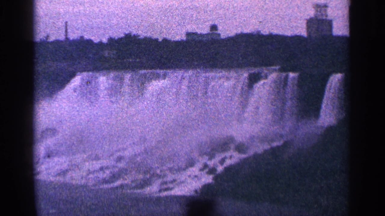 Niagara Falls with mist and distant structures across the top of the waterfall.